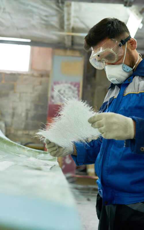 Portrait of mature man wearing protective mask repairing boat while working in yacht workshop, copy space